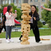 Family play a game of giant Jenga, outdoors in a park.