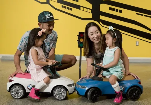 kids riding toy cars with their parents around them 
