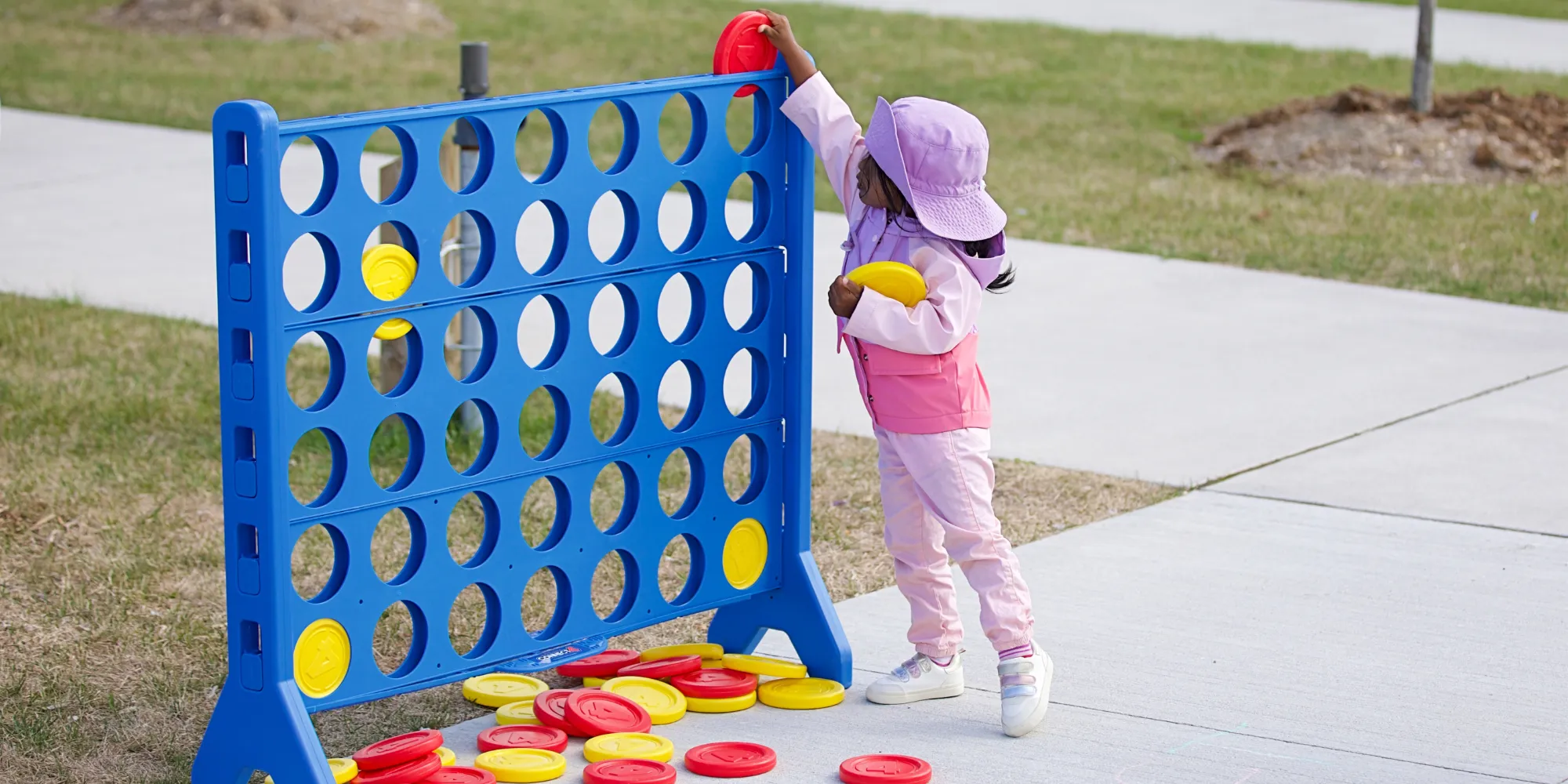Child on pavement playing with a large Connect Four board.