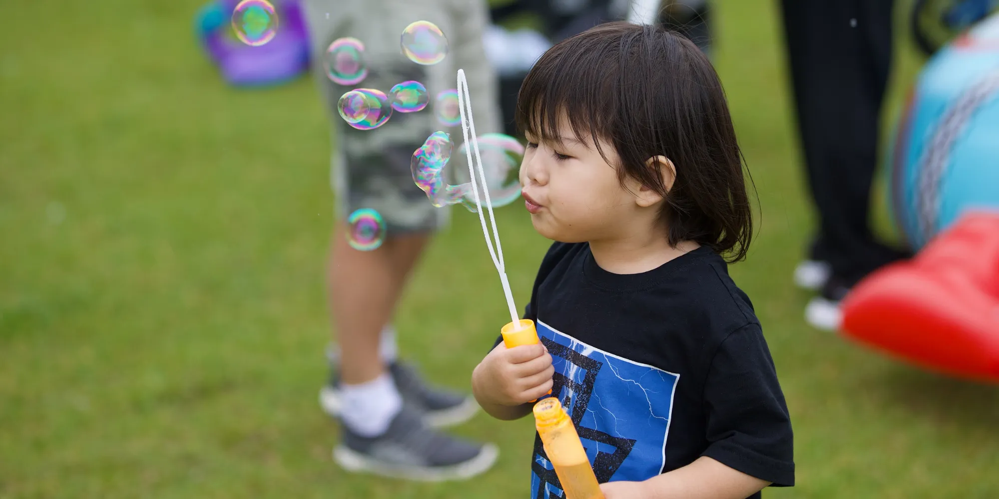 Young child blowing bubbles in a field.